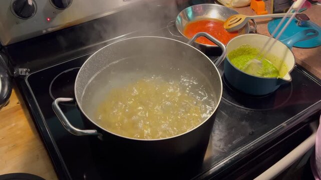 Pasta boiling in a pot on a stove top while sauce is stirred in background 