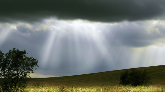 Sunbeams breaking through heavy dark clouds above a tranquil field, theme of divine providence and hopefulness
