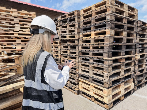 Stacked wooden shipping pallets in warehouse with worker using mobile phone - Supply chain logistics concept