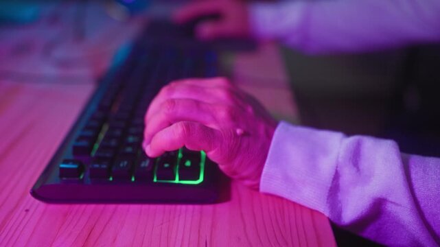 Man middle age typing on a backlit gaming keyboard, fingers pressing keys and right hand on mouse at a desk in studio; focus immersion.
