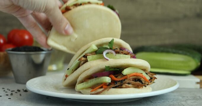 Woman taking delicious gua bao at grey table, closeup