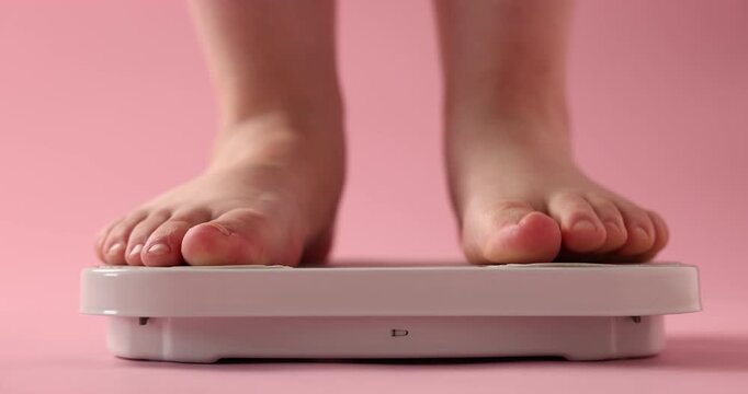 Overweight woman stepping on scale against pink background, closeup