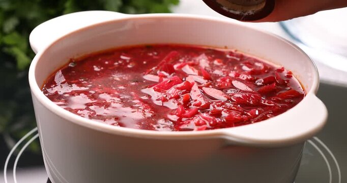 Woman adding spices to borscht while cooking at stove, closeup