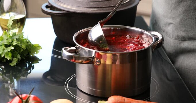Woman taking borscht from pot with ladle at stove, closeup
