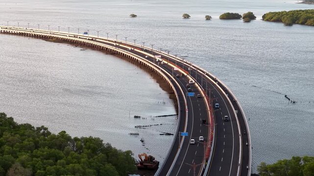 Aerial view of Bali Mandara Toll Road with cars driving across the bridge surrounded by mangrove forests and calm water in Kabupaten Badung, Bali, Indonesia.
