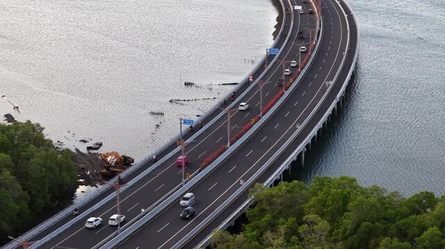 Aerial view of the Mandara Toll Road over the water with cars driving along the highway near mangroves in Kabupaten Badung, Bali, Indonesia.