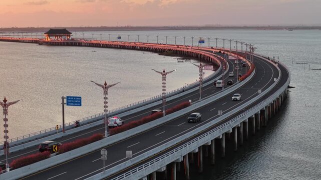 Aerial view of the Bali Mandara Toll Road with cars driving over the water at sunset in Kabupaten Badung, Bali, Indonesia.