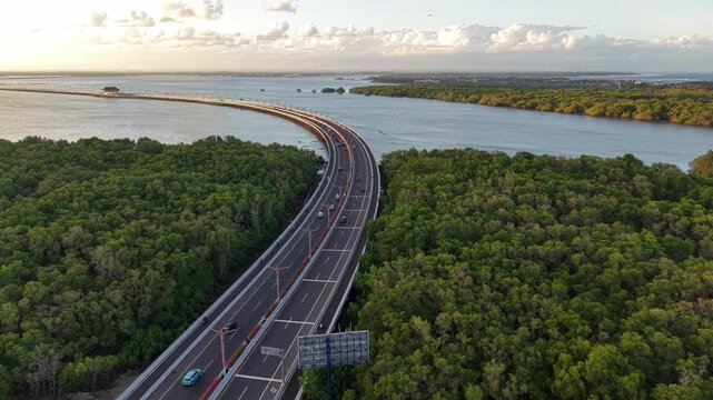 Aerial view of the Bali Mandara Toll Road winding through lush mangrove forests in Kabupaten Badung, Bali, Indonesia.