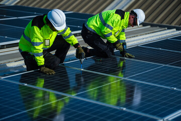 Fototapeta premium A solar installation engineer in a white helmet and high visibility vest confidently kneels on the evening array reporting over the radio on a commercial factory rooftop photovoltaic.