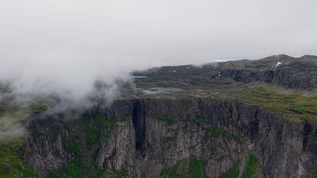 Aerial view of dramatic cliffs and mountain gorge with low hanging clouds over the rugged landscape in Norway.