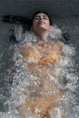 Fototapeta premium Woman in a yellow bikini reclining in bubbling spa water with eyes closed