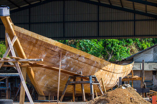 A large traditional wooden fishing boat under construction inside a shipyard