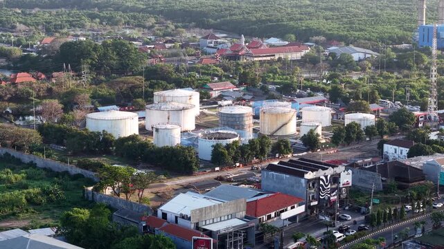 Aerial view of Pertamina Fuel Depot with large white storage tanks surrounded by lush trees and urban infrastructure in Kecamatan Denpasar Selatan, Bali, Indonesia.
