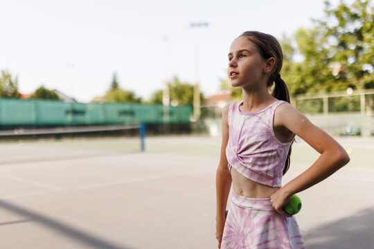Young girl practices tennis on a sunny day at a local court focusing on her next move as she holds a tennis ball in hand ready to serve or rally
