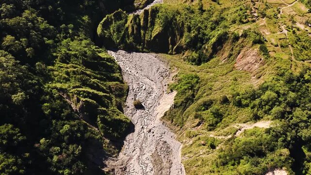 Aerial view of a rocky riverbed winding through lush green hills and steep slopes in Makassar, South Sulawesi, Indonesia.
