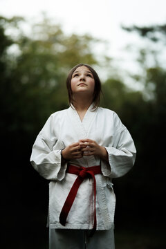 Young girl in karate gi with red belt standing outdoors looking up with calm focus during martial arts practice