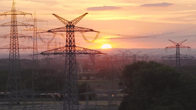 Aerial view of Amprion-Umspannwerk with high-voltage electricity pylons silhouetted against a golden sunset in Pfungstadt, Hessen, Germany.