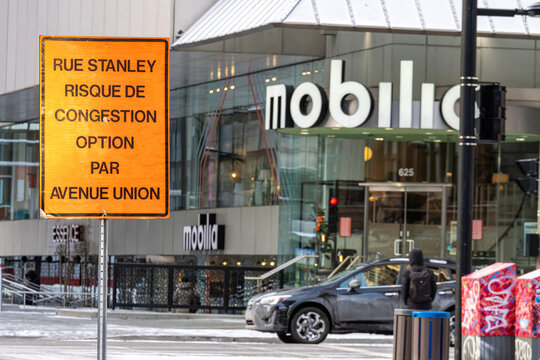 MONTREAL, CANADA, 22 December 2025 : Warning Sign in French, Urban Street Scene, Traffic Congestion, Winter City Street, Hooded Pedestrian, Modern Building, Montreal Canada