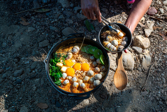 Outdoor lifestyle concept showing someone dishing up delicious instant noodles from a large pot, real image, not AI generated.