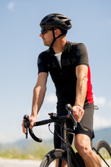Fototapeta premium Cyclist in a red and black jersey takes a break on a sunny day while resting on a road bike at a scenic location