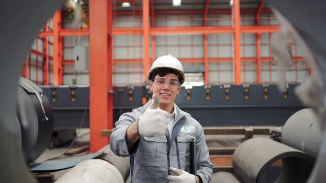 Smiling factory engineer holding tablet and showing thumbs up gesture
