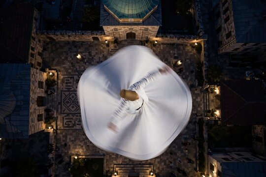 Aerial top view of a whirling dervish performing a traditional Sufi dance in a historical stone courtyard at night with motion blur