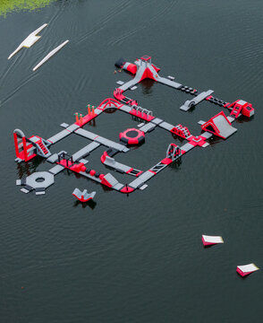 Aerial view of an inflatable water park with various obstacles, slides, and platforms floating on a calm lake in Vilnius, Vilniaus apskritis, Lithuania.