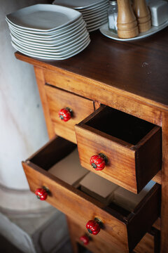 Well-organized wooden drawer with red knobs and neatly stacked plates in a cozy kitchen setting - vertical