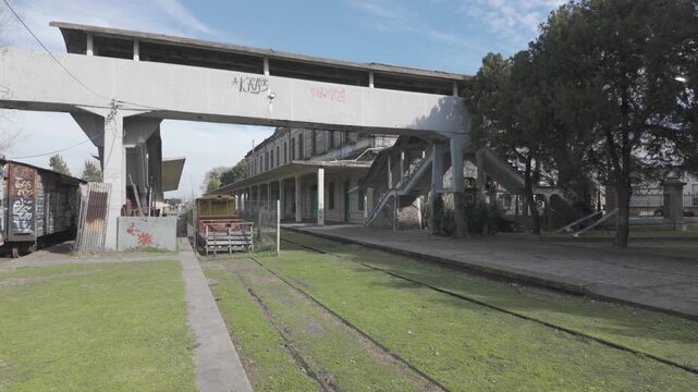 Zoom-in shot showing the concrete footbridge, platforms, and abandoned tracks at historic La Plata El Provincial station, Argentina. D-Log M, 10-bit color, flat log profile.