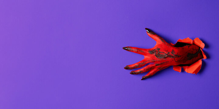 Halloween. Scary red hands with long nails break through vibrant purple backdrop