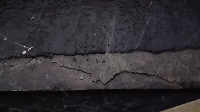 Close up shot of a deep crack and damage on a dark weathered asphalt or concrete ground surface