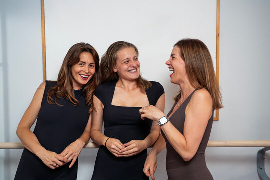 Three smiling women in athletic jumpsuits share a joyful moment together while posing in a gym, closeup shot 