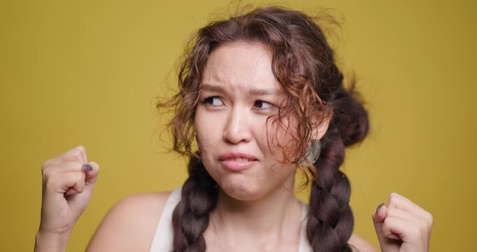 Young Kazakh woman expressing anger with dramatic facial gestures against a yellow background