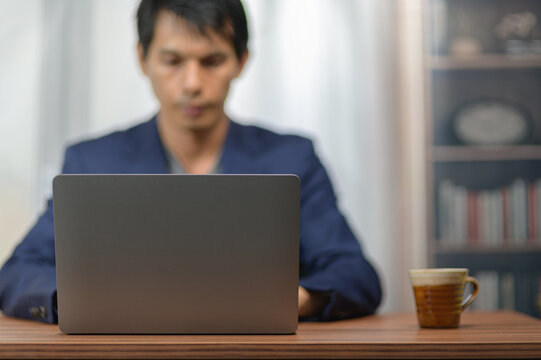 Person Using Laptop Computer at Desk in Home Office with Bookcase and Coffee Mug