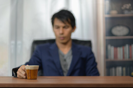Businessman Sitting at Desk Holding Coffee in Modern Office Environment