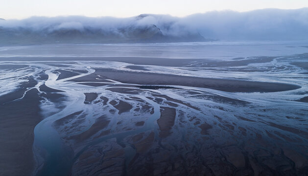title": "Aerial View of Serene Coastal Landscape with Misty Mountains and Tranquil River Delta at Dawn or Dusk", "description": "This captivating aerial photograph captures the breathtaking beauty of