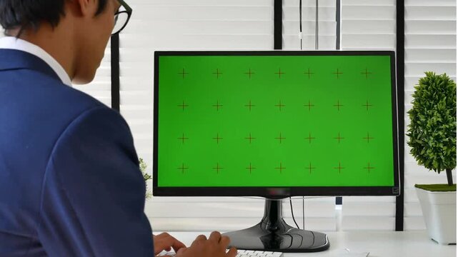 Businessman working on computer with green screen display chroma key mockup in modern office