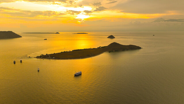 Aerial view of Pulau Kenawa surrounded by calm waters and boats during a golden sunset, Poto Tano, West Nusa Tenggara, Indonesia.