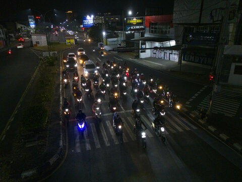Aerial view of Perempatan Kentungan at night with many motorcyclists waiting at a traffic light, illuminated by headlights in Kecamatan Mlati, Daerah Istimewa Yogya, Indonesia.