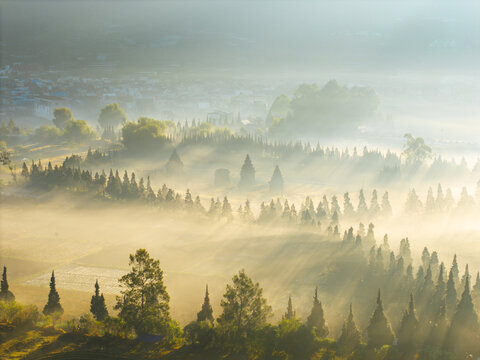 Aerial view of Candi Arjuna temple complex surrounded by morning mist and sun rays in the Dieng Plateau, Indonesia.