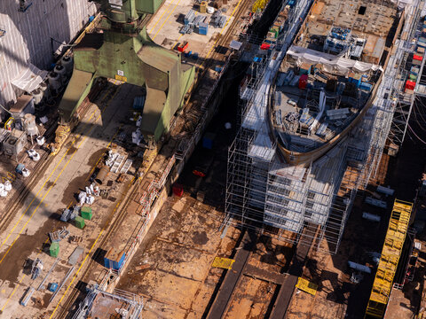 Aerial view of a ship under construction in a dry dock with scaffolding and large industrial cranes in a shipyard in Gdansk, Poland.