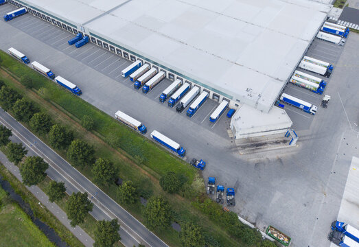 Aerial view of a large logistics warehouse facility with numerous semi-trucks parked at loading docks and maneuvering in the yard in Culemborg, Gelderland, Netherlands.