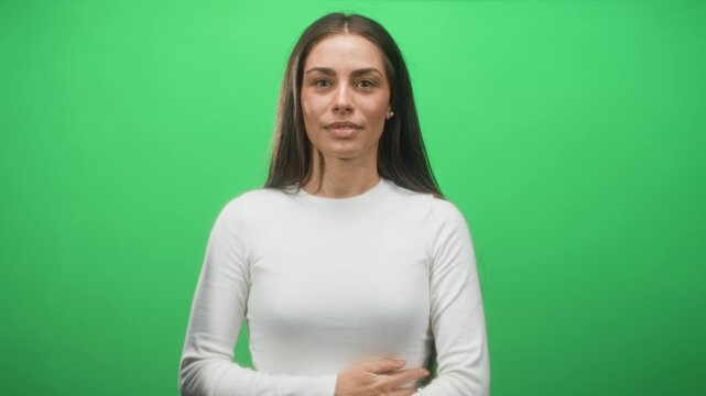 Woman holding hand on abdomen with a subtle wince against a green screen studio backdrop; mild discomfort.