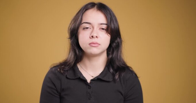 Serene young woman with neutral expression against a warm yellow background