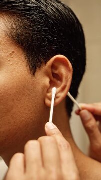 Close up of a man cleaning his ear canal with a cotton swab and risking potential ear health and hearing loss damage