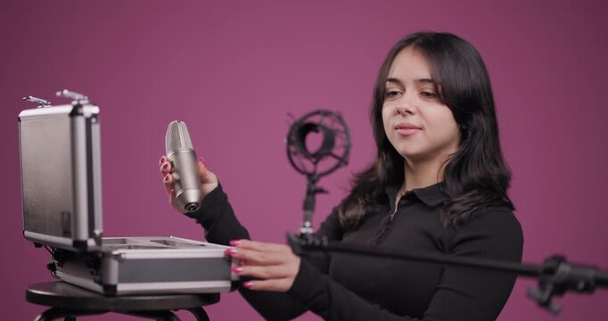 Young woman professionally setting up recording equipment in studio. Microphone on a stand.
