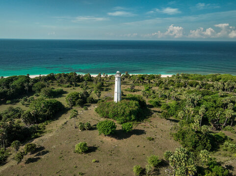 Aerial view of the Nuca Molas lighthouse surrounded by lush tropical vegetation and palm trees on the coast of Satar Mese Barat, East Nusa Tenggara, Indonesia.