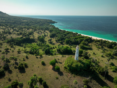 Aerial view of the Nuca Molas lighthouse standing amidst lush greenery and palm trees along the turquoise coastline of Satar Mese Barat, East Nusa Tenggara, Indonesia.