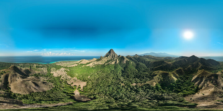Aerial view of Nuca Molas island featuring rugged green hills, lush tropical vegetation, and clear blue ocean waters under a bright sunny sky in Satar Mese Barat, East Nusa Tenggara, Indonesia.