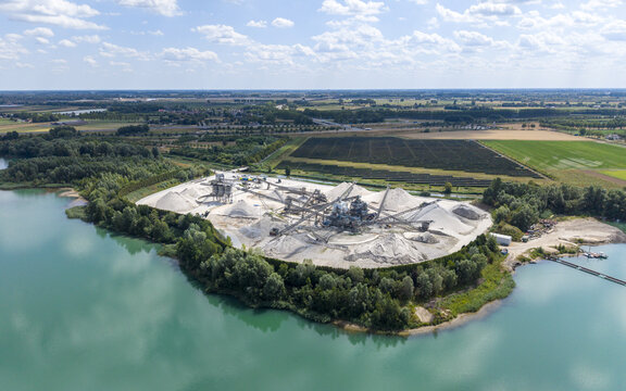 Aerial view of K3 Industriezand B.v. sand extraction site situated on the shore of a turquoise lake, surrounded by lush greenery and agricultural fields in Echteld, Gelderland, Netherlands.